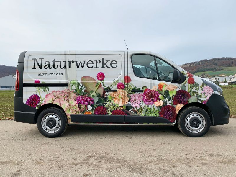 Transportbus mit seitlicher Beschriftung Naturwerk und Blumenmotiv.