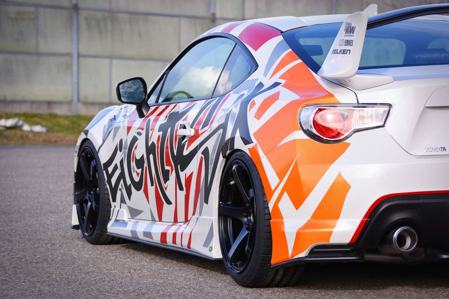 Toyota Sportwagen weiss teilfoliert mit grafischem Motiv in orange, rot und Aufschrift in Schwarz.