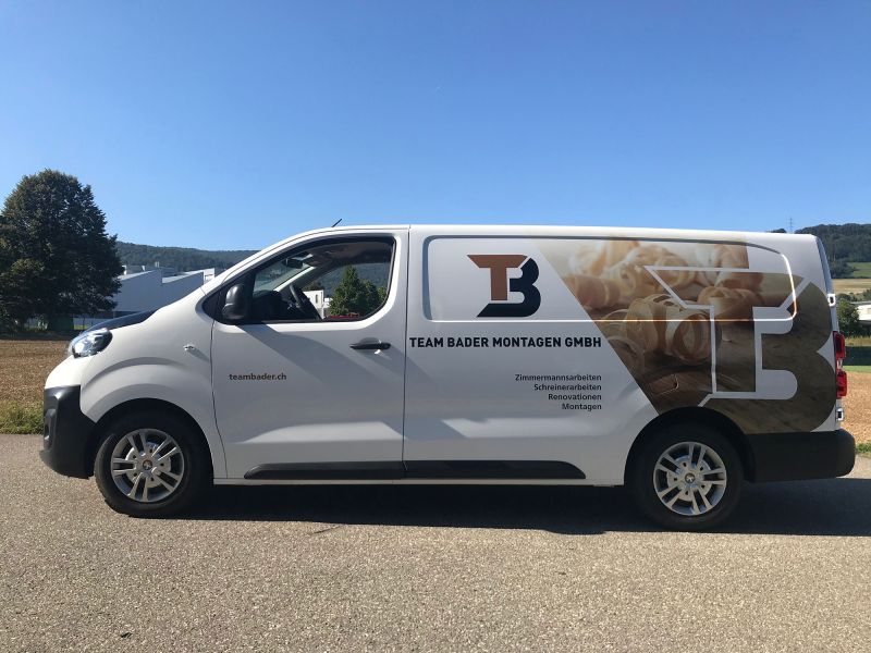 Transportbus mit seitlicher Beschriftung Team Bader Montagen und Holzmotiv