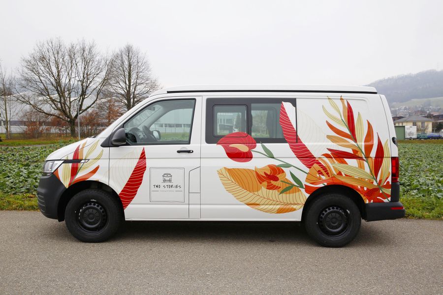 Camper Bus Two Stories mit seitlicher Beschriftung Blumen und Blätter.